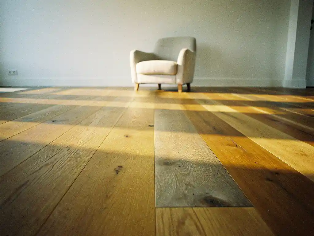 Brede eiken plankvloer in honingbruine en asgrauwe tinten, verlicht door goudkleurig middaglicht in een minimalistisch Nederlands interieur.